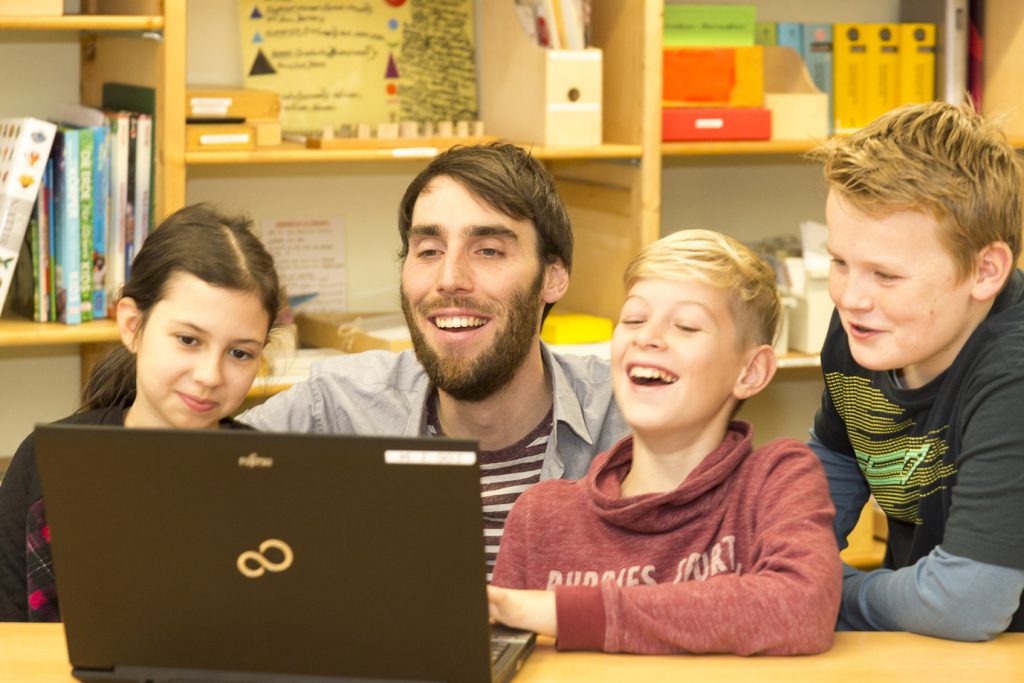 Mehrere Schüler mit Lehrer am Laptop